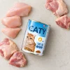 Flat-lay 20035 CATY Drůbeží kousky v omáčce 415 g se syrovým kuřecím masem na světlé kuchyňské lince. Label ref = BaseLinker e-shop packshot.