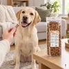 Lifestyle SKU 204603 (Akinu Kosti sušenka se zinkem 1 000 g) — obývák, labrador čeká na sušenku z ruky majitele, sáček na konferenčním stolku, evergreen, odpoledne, útulný mood. Maketa v Heliosu chybí — reference: sólo packshot a4745c6b (job ce4bbb7f) + BaseLinker foto 1be2e52c. 2k 1:1, vybrána v1 ze 2.