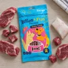 Flat-lay shora: sáček Jehněčí sendvič 176225 uprostřed, kolem syrové jehněčí maso (plátky + kostičky) a kousek tresky, podklad kuchyňská linka