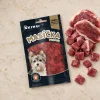 Úprava flat-lay (parent ed43c321): odstraněna dýně, vedle sáčku pouze syrové kachní maso. Travertin, top-down.