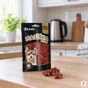 Lifestyle: sáček Akinu Masíčka Premium Kachní maso 75 g na běžné české kuchyňské lince (laminát, bílé skříňky), pár pamlsků před sáčkem.