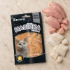 Flat-lay Akinu Masíčka Premium Kuřecí plátky pro kočky mramorované 50 g (282054) — sáček mírně mimo střed na matném travertinu, syrové kuřecí (plátky + kostičky) a treska asymetricky v jednom rohu. Varianta f1 ze 4. Surovinová reference = AI generace syrového kuřecího a tresky (job 1c5e8449); kompoziční reference řady v Content DB nenalezena.